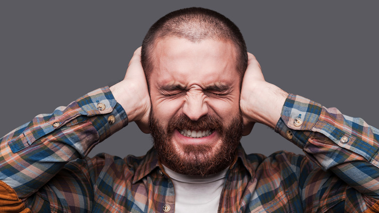 A man covering his ears in frustration, symbolizing the outdated problem of loud laptop fan noise.
