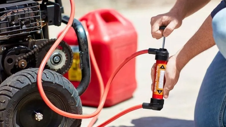 A red manual hand pump being used to transfer fuel from a plastic container.