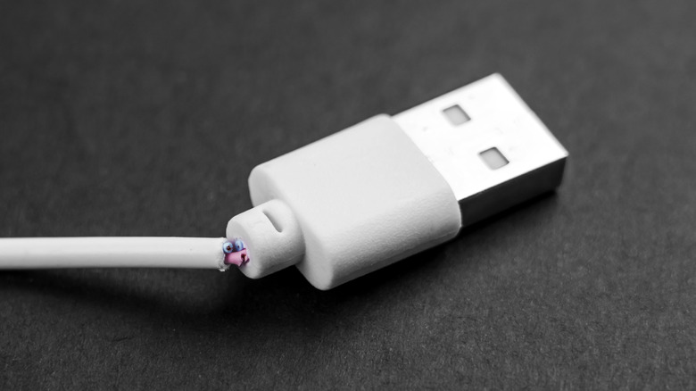 A close-up of a USB cable with frayed insulation and exposed internal copper wiring.