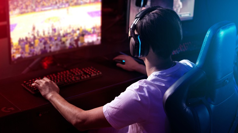 A young man wearing a headset sitting at a computer desk engaged in video gaming.