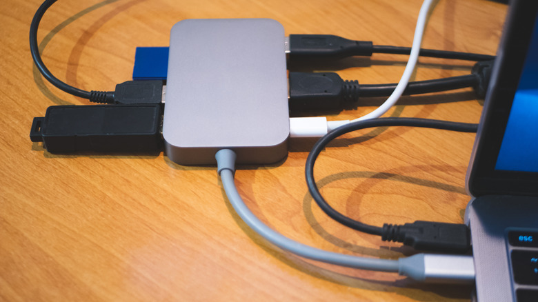 A multi-port USB hub with several cables connected, sitting on a desk next to a laptop.