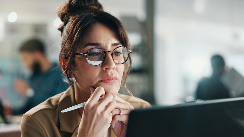 A professional woman thoughtfully looking at her laptop screen while working in a modern office.