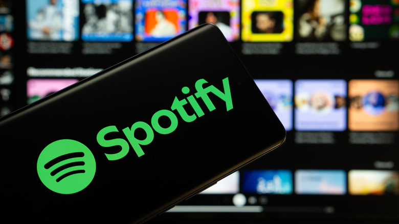 A smartphone held in front of a screen displaying the Spotify logo.