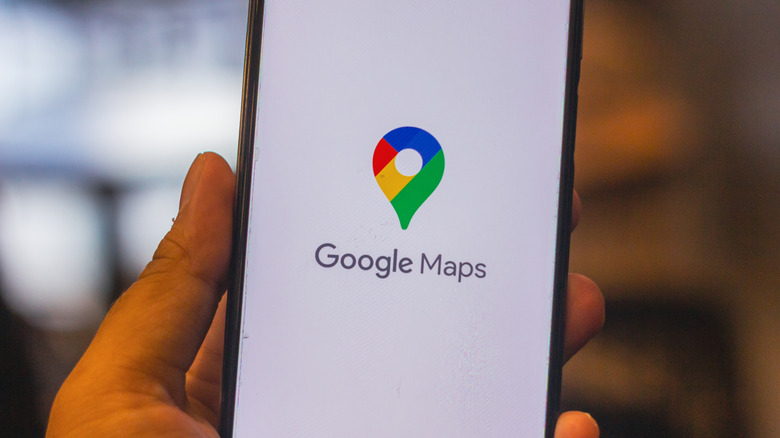 A hand holding a smartphone with the Google Maps icon visible on the screen.