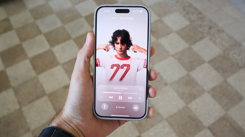 iOS 26 lock screen featuring a translucent Apple Music album cover and refined notification stack.