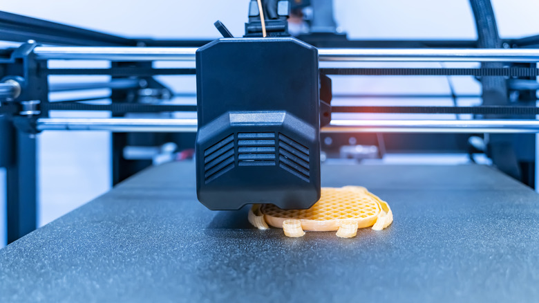 Close-up of a 3D printer nozzle depositing filament on a build plate.