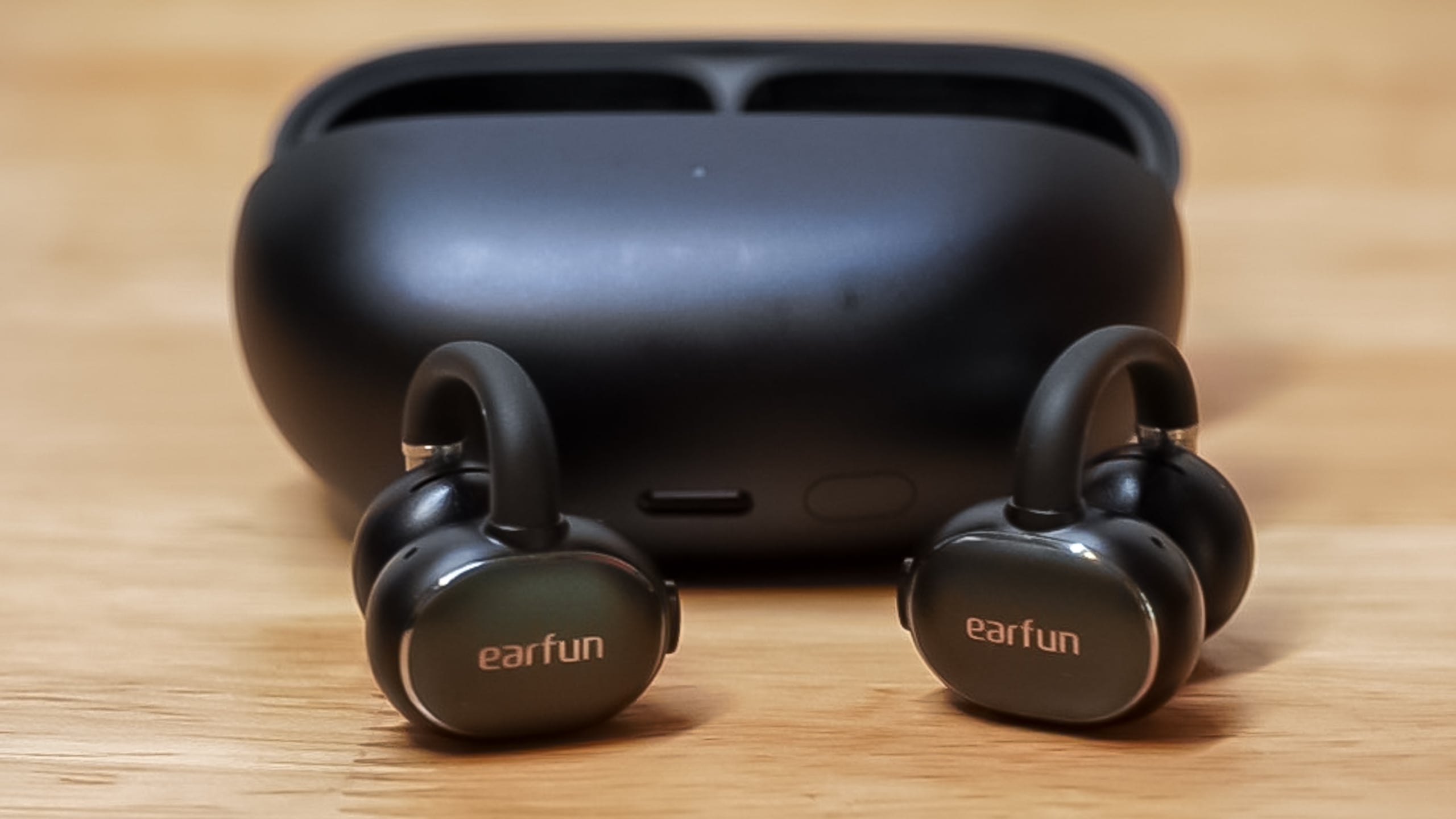 The EarFun Clip 2 earbuds alongside their charging case on a flat surface.