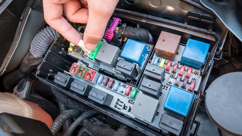 A person's hand removing a fuse from the vehicle's internal fuse box.