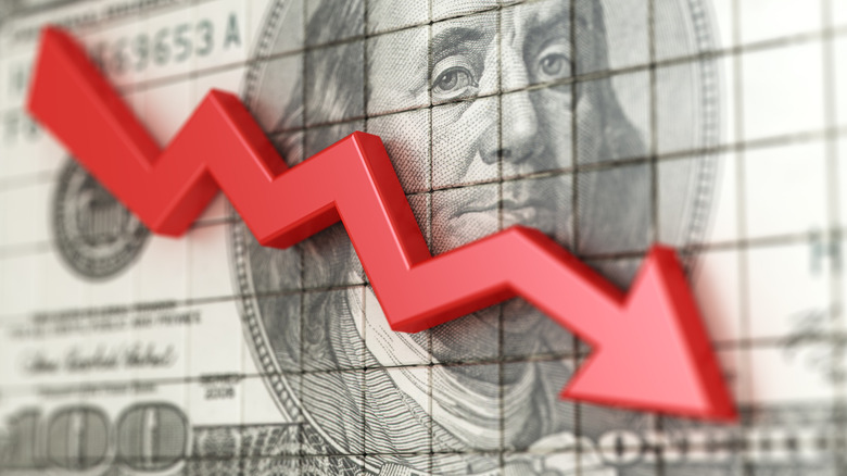 A hundred dollar bill with a red stock market downward arrow overlaid on it.