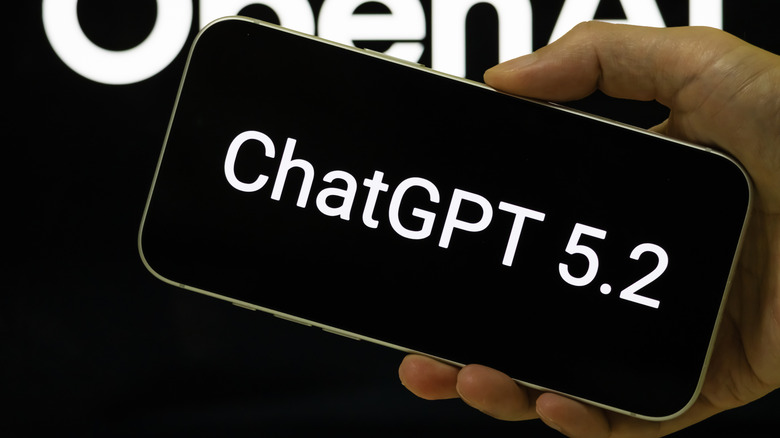 A hand holding a smartphone displaying the ChatGPT 5.2 interface against an OpenAI logo background.