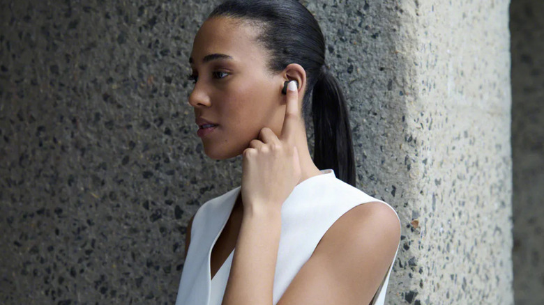 A woman interacting with the touch control sensor on the side of a Sony WF-1000XM6 earbud.