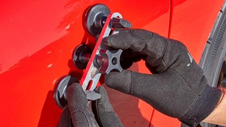 A person using a plastic dent removal bridge tool on a silver car door.