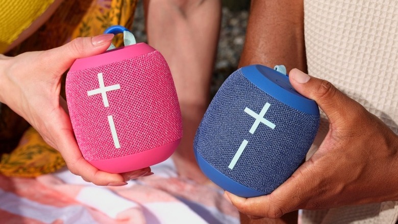 Two hands holding the Ultimate Ears Wonderboom 4 speaker in two colors.