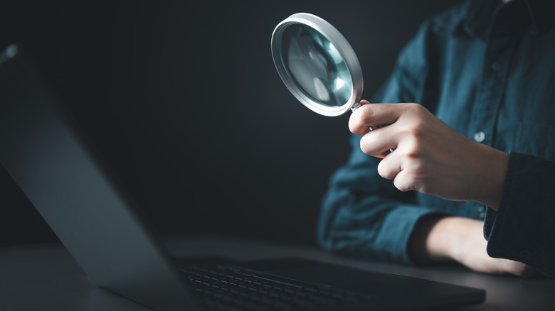 A magnifying glass held over a laptop screen, emphasizing the search for high-value electronics.