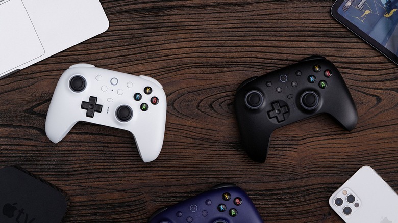 A collection of colorful 8BitDo controllers arranged on a wooden table with gaming peripherals.
