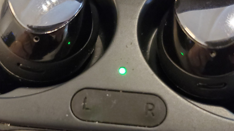A detailed close-up of the charging case's internal LED indicator light glowing between the earbud cradles.