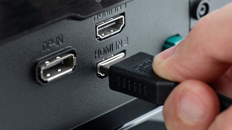 A close-up of a person's hand plugging an HDMI cable into a port.
