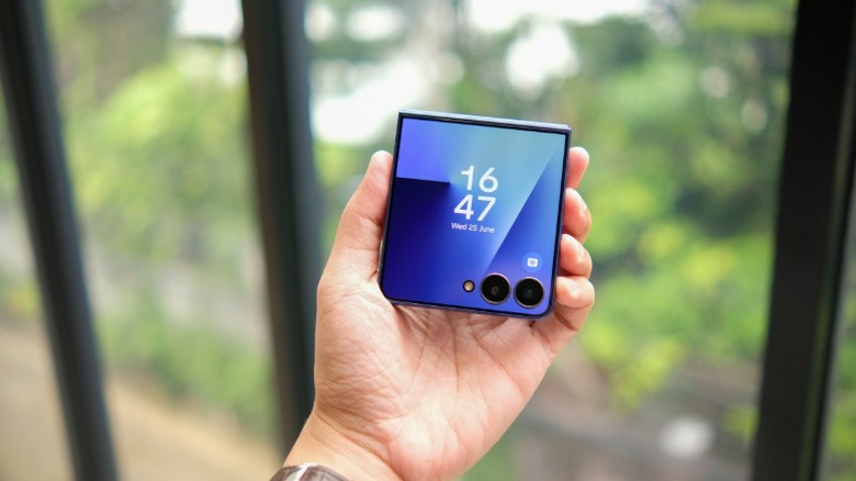 A hand holding a foldable Samsung Galaxy Z Flip7 in its partially folded state.