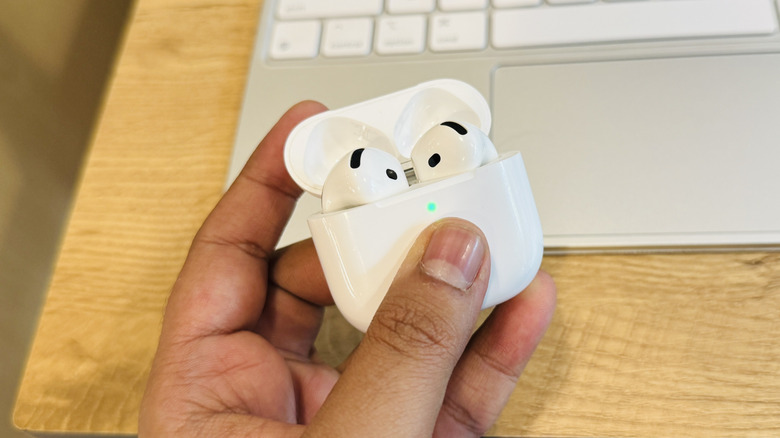 A thumb pressing the capacitive sensor area on the front of the AirPods 4 charging case.