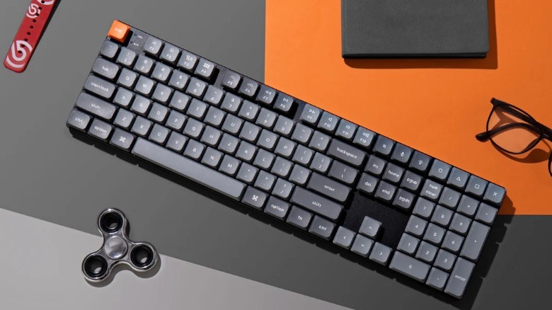 A Keychron K5 Max mechanical keyboard on a desk alongside lifestyle accessories.