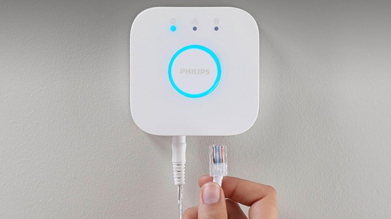A person connecting a white Philips Hue Bridge to a network switch using an Ethernet cable.