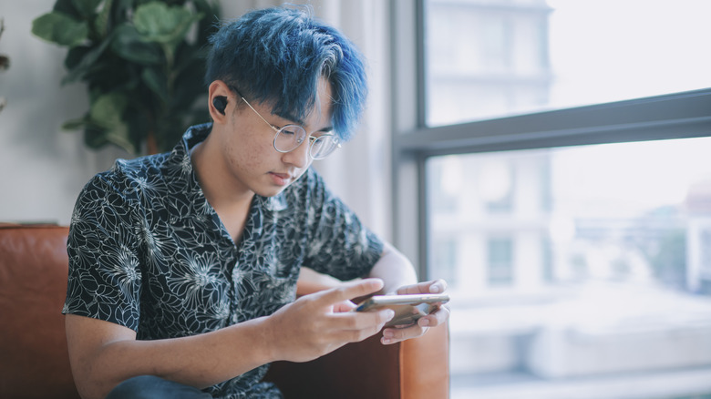A person using a smartphone to control wireless earbuds while sitting comfortably.