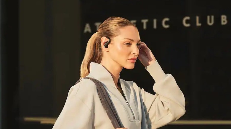 Close-up of a person wearing the white Beats Powerbeats Pro 2 earbuds while adjusting the touch controls.