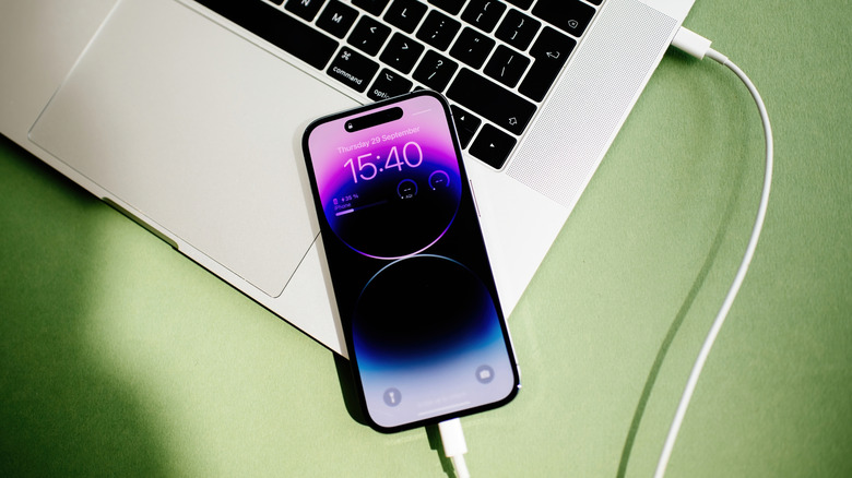 An iPhone 15 Pro connected to a MacBook Pro via a white USB-C cable.