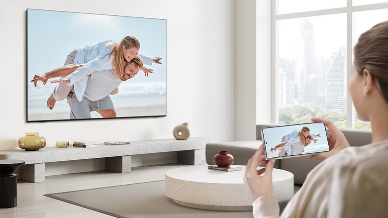 A person holding a phone that is wirelessly mirroring its display to a nearby smart TV.