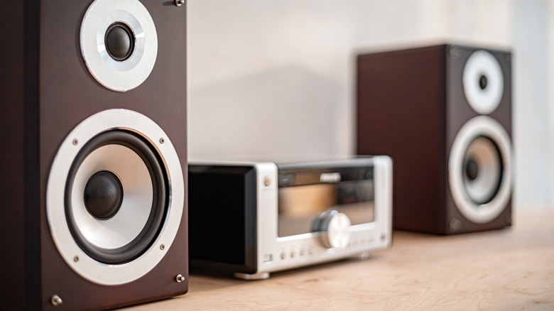 A clean, minimalist audio setup with two wooden bookshelf speakers and a central receiver on a desk.