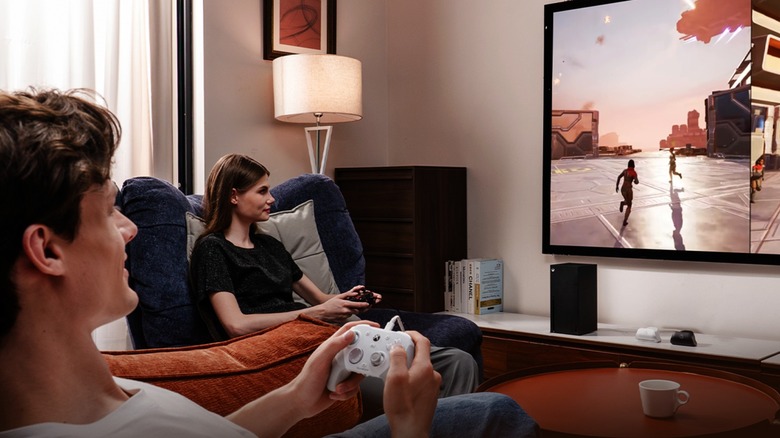 Two people playing a split-screen game on a couch using GameSir controllers.