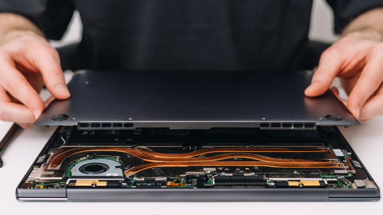 Close-up of a laptop with its bottom case removed, showing copper heat pipes and dual cooling fans.