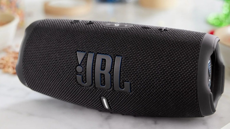 A JBL Charge 5 Wi-Fi SE speaker placed on a modern marble countertop, emphasizing its sleek yet durable build. [3]