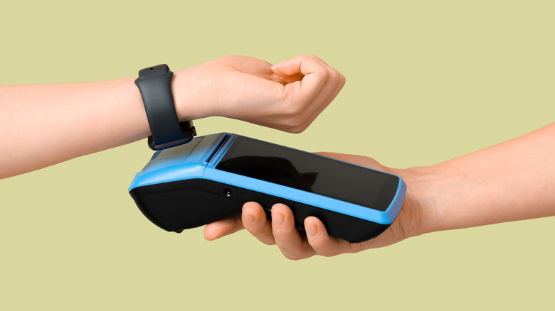 A person using a smartwatch to complete a contactless payment at a retail terminal.