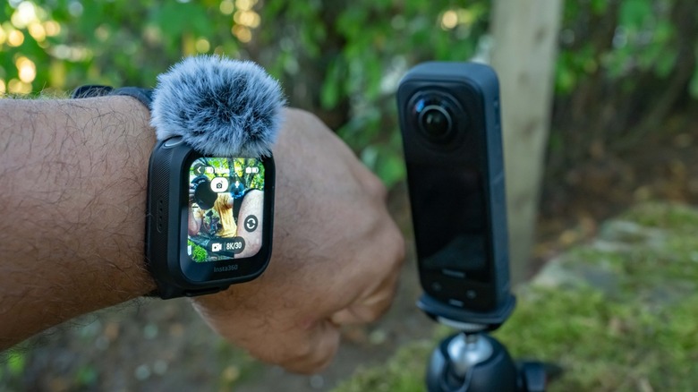 The Insta360 X5 GPS Preview Remote worn on a wrist next to the camera with a deadcat windmuff attached.