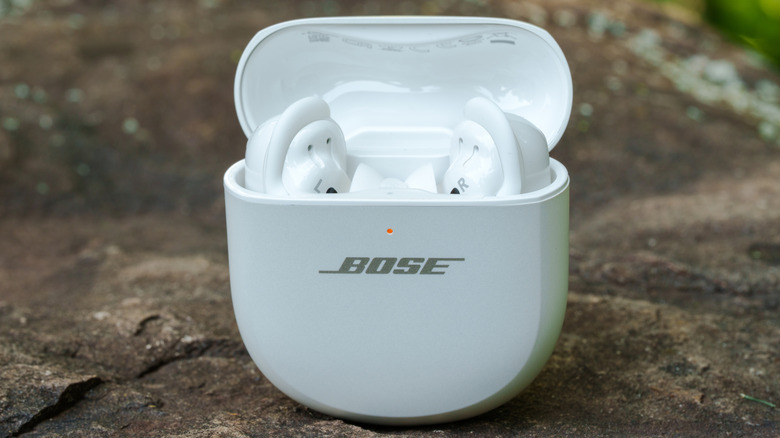 The Bose QuietComfort Ultra Earbuds resting on a rock in an outdoor environment.