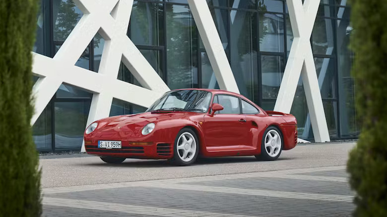 A classic red Porsche 959 parked in front of a modern building, highlighting its status as a production icon.