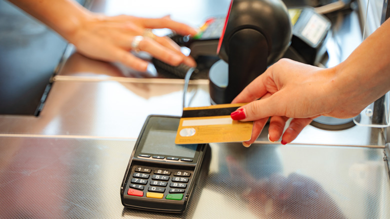 A customer inserting a credit card into a payment terminal at a grocery store checkout.