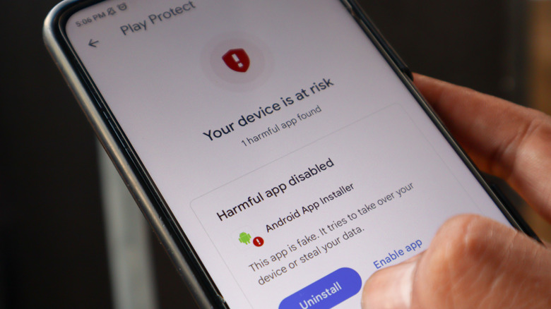 A hand holding a smartphone with a Google Play Protect malicious app warning on the screen.