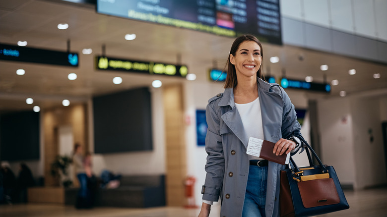 A traveler walking through a bright airport terminal carrying a suitcase.