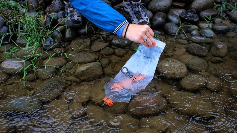 A camper filling a flexible Cnoc Vecto water bag from a shallow stream.