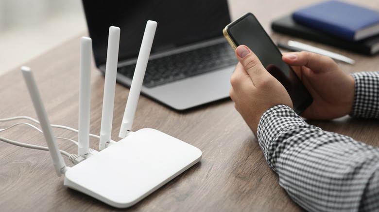 A person using a laptop and smartphone near a wireless home router.