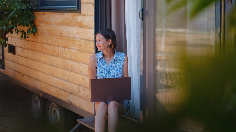 A woman sitting on a bench outdoors using a laptop to work remotely.
