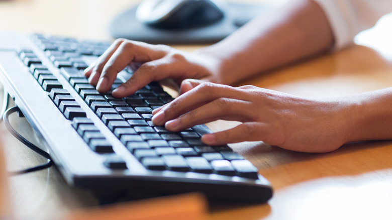 A person wearing protective gloves wiping down a laptop keyboard with a microfiber cloth.