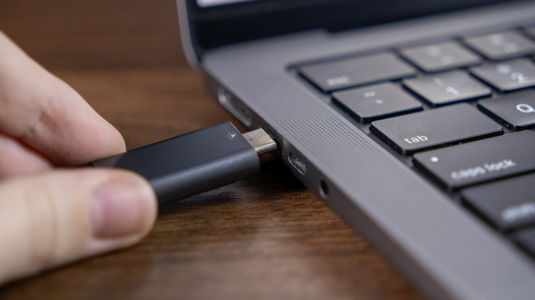 A person carefully inserting a USB-A cable into a laptop port.