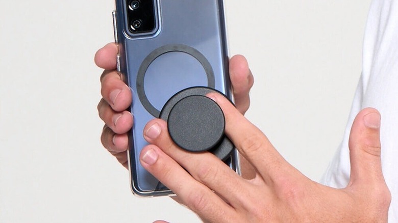 A person's hand holding an Android phone equipped with a magnetic PopSocket grip.