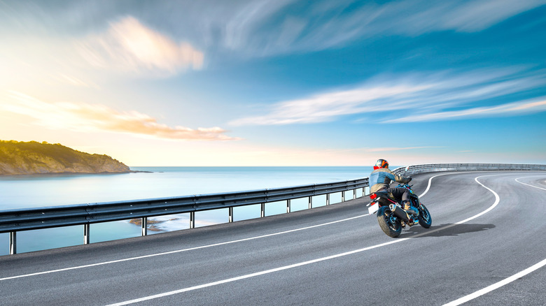 A motorcyclist riding on a scenic highway near a cliff's edge.