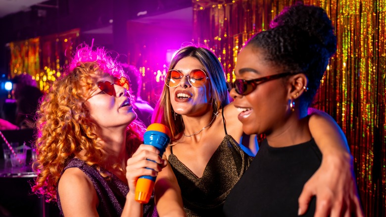 A group of friends laughing and singing together with a colorful karaoke microphone.