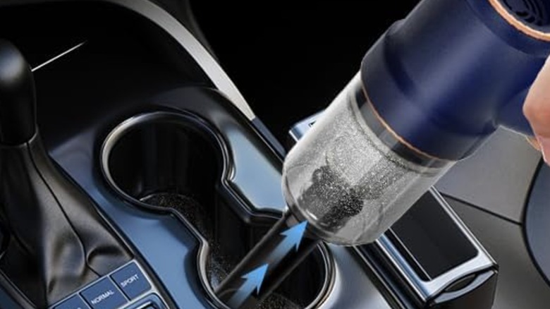A close-up shot of the KMM handheld car vacuum cleaning dirt out of a vehicle cupholder.