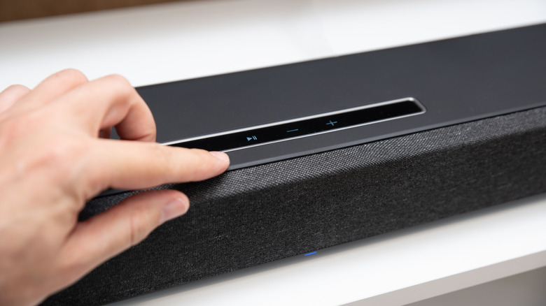 Close-up of a hand using the control panel on a soundbar to navigate settings.